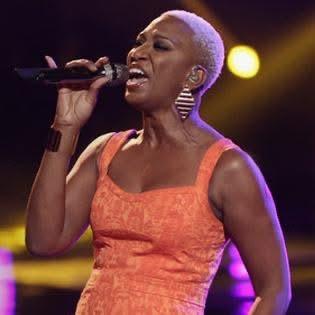 Sisaundra Lewis singing into a microphone in an orange dress